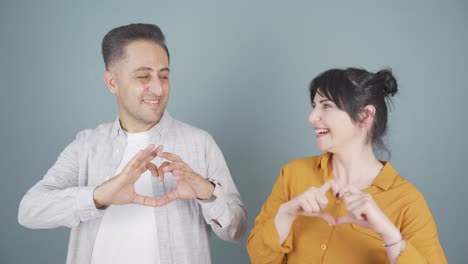 Couple-making-heart-sign-at-camera.